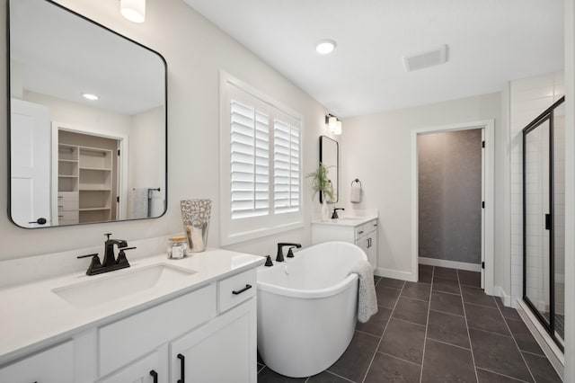 bathroom featuring a stall shower, a soaking tub, a walk in closet, two vanities, and recessed lighting