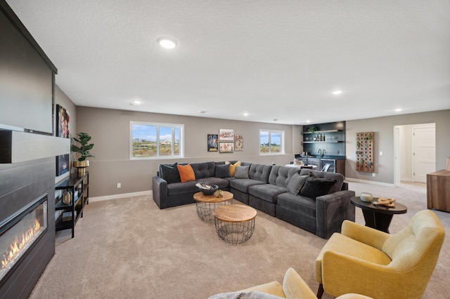 living area featuring light colored carpet, a glass covered fireplace, baseboards, recessed lighting, and a textured ceiling