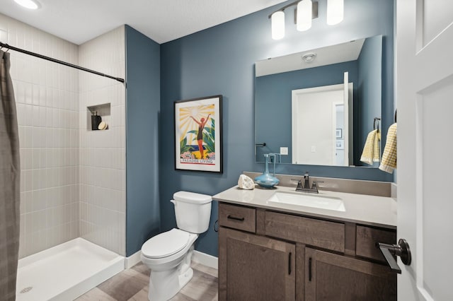 bathroom featuring a stall shower, toilet, vanity, baseboards, and wood finished floors