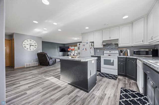 kitchen with white appliances, under cabinet range hood, light wood-style flooring, white cabinetry, and recessed lighting