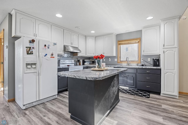 kitchen with white appliances, under cabinet range hood, white cabinetry, a center island, and a sink