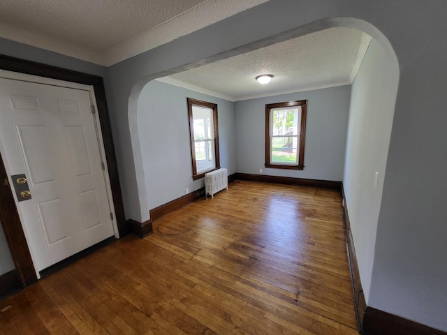 empty room featuring radiator, arched walkways, a textured ceiling, baseboards, and wood-type flooring