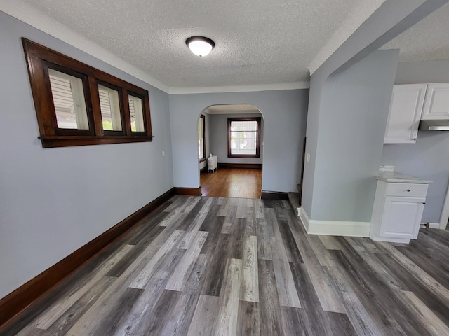 hallway featuring a textured ceiling, arched walkways, wood finished floors, and baseboards
