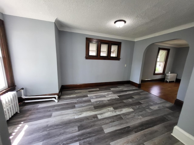 empty room featuring radiator heating unit, arched walkways, a textured ceiling, and wood finished floors