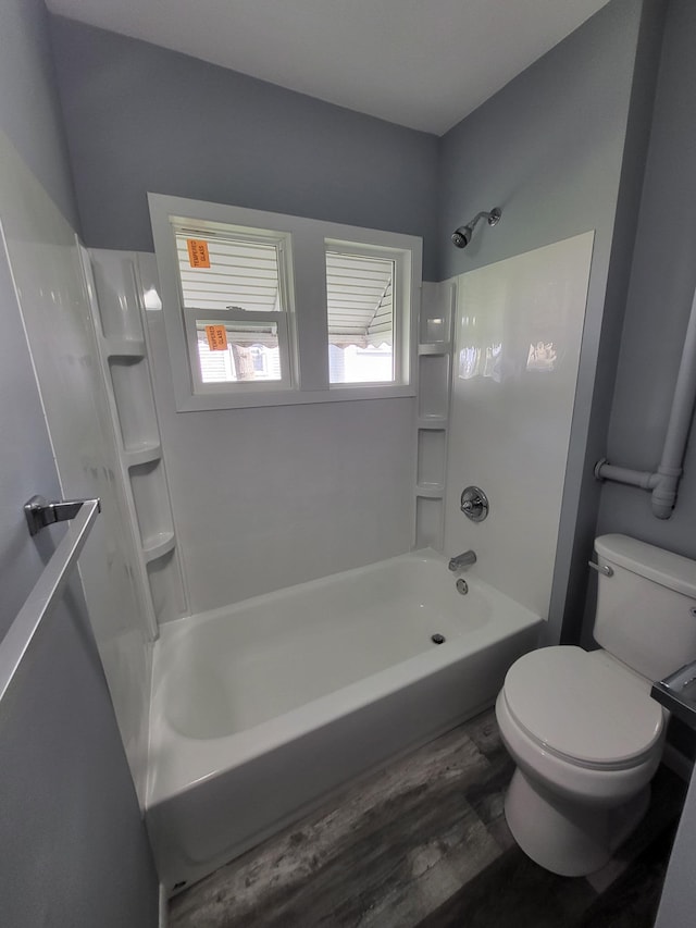 full bath with washtub / shower combination, toilet, and wood finished floors