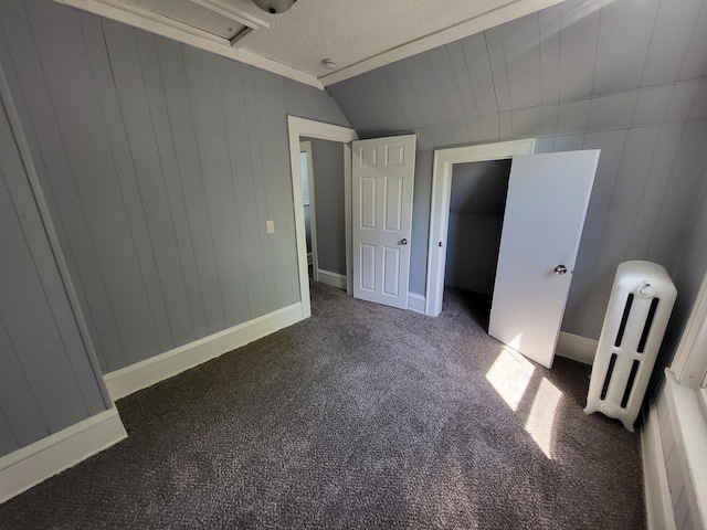 unfurnished bedroom featuring carpet, vaulted ceiling, a textured ceiling, radiator heating unit, and baseboards