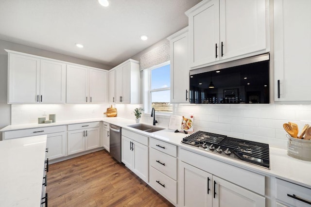 kitchen with stainless steel appliances, white cabinets, a sink, decorative backsplash, and light countertops