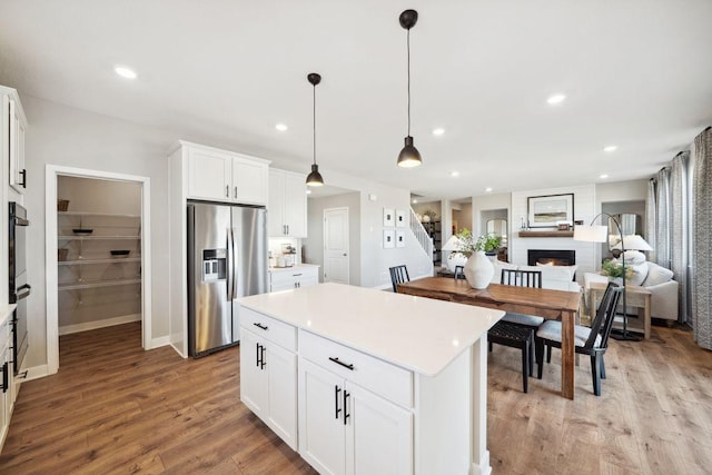 kitchen with stainless steel refrigerator with ice dispenser, a warm lit fireplace, open floor plan, light wood finished floors, and white cabinets