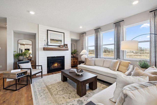 living area featuring wood finished floors, a large fireplace, a textured ceiling, recessed lighting, and baseboards