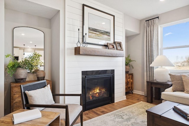 living area with wood finished floors, a glass covered fireplace, recessed lighting, and baseboards