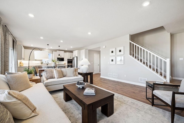 living room featuring stairs, light wood finished floors, recessed lighting, and baseboards