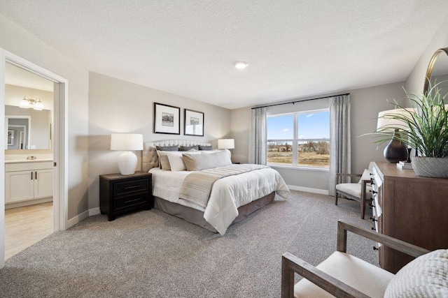 bedroom with light carpet, baseboards, a sink, a textured ceiling, and ensuite bath