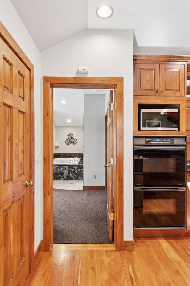 12640 Fawn Lake Rd, Crosslake, MN 56442 - kitchen with stainless steel microwave, lofted ceiling, light wood-style flooring, baseboards, and brown cabinets