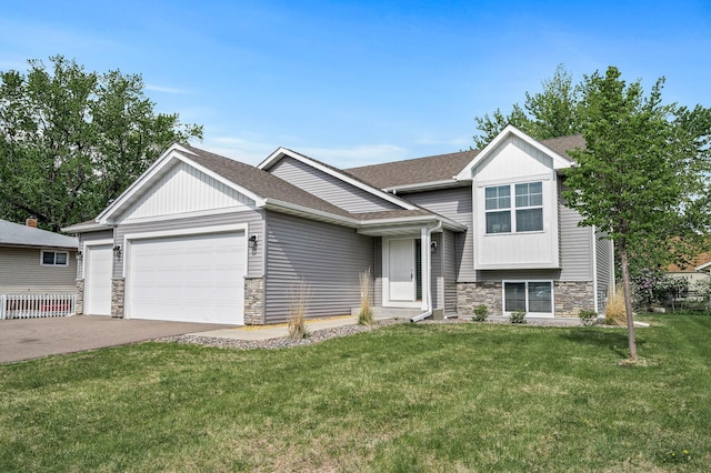 split level home featuring stone siding, a garage, a front yard, concrete driveway, and roof with shingles