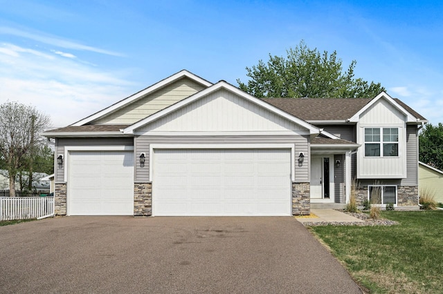 split level home featuring stone siding, an attached garage, driveway, and roof with shingles