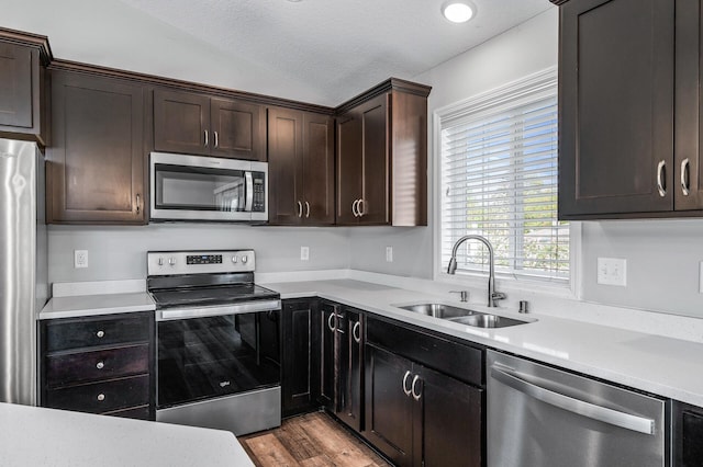 kitchen with appliances with stainless steel finishes, a sink, lofted ceiling, light countertops, and dark brown cabinetry