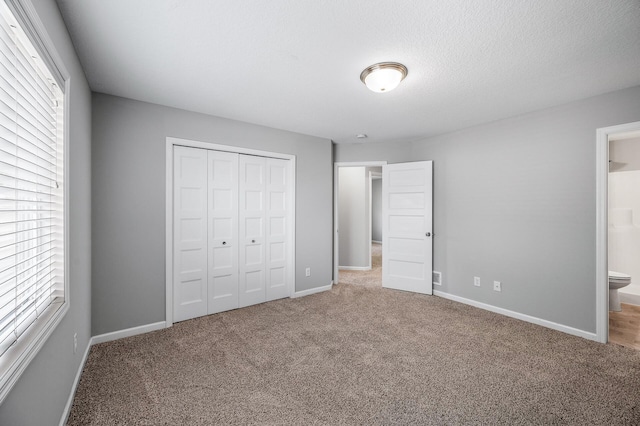 unfurnished bedroom with carpet floors, a closet, baseboards, and ensuite bath