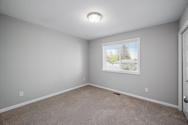 carpeted spare room featuring a textured ceiling and baseboards