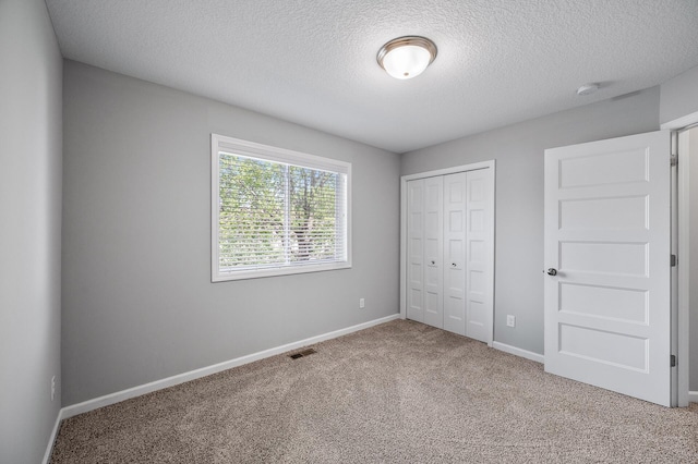 unfurnished bedroom with carpet flooring, a textured ceiling, baseboards, and a closet