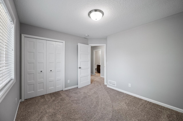 unfurnished bedroom featuring carpet, a textured ceiling, a closet, baseboards, and multiple windows