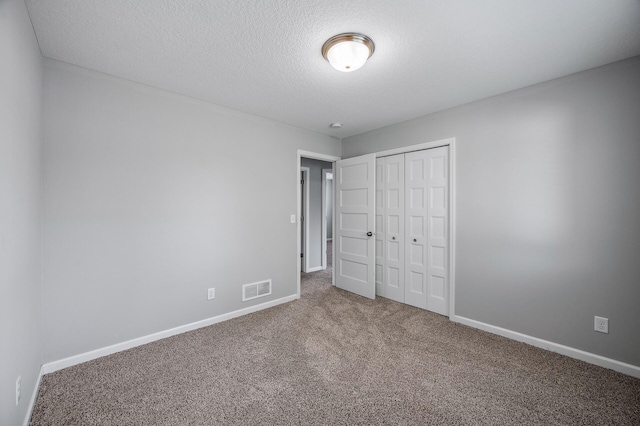 unfurnished bedroom featuring carpet, a textured ceiling, a closet, and baseboards