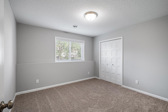 unfurnished bedroom featuring a closet, a textured ceiling, carpet floors, and baseboards
