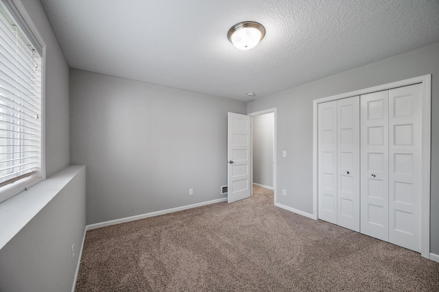 unfurnished bedroom featuring carpet flooring, baseboards, a closet, multiple windows, and a textured ceiling