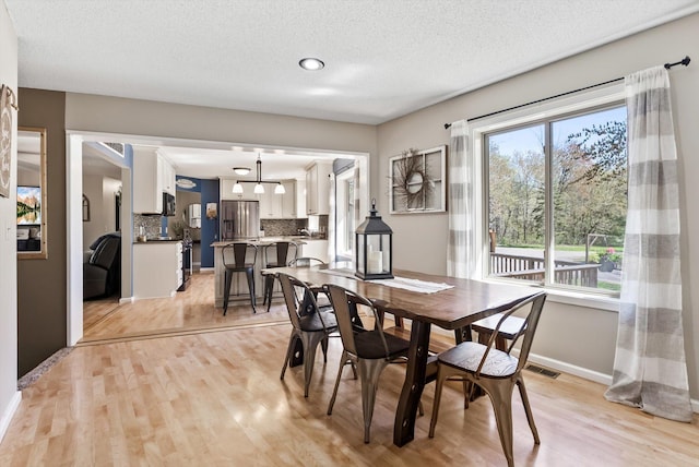 dining room featuring light wood-style floors, baseboards, and a textured ceiling