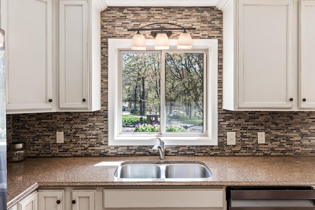 kitchen with a sink, dishwasher, backsplash, and white cabinetry