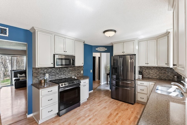 kitchen with stainless steel appliances, a sink, decorative backsplash, a textured ceiling, and light wood-style flooring