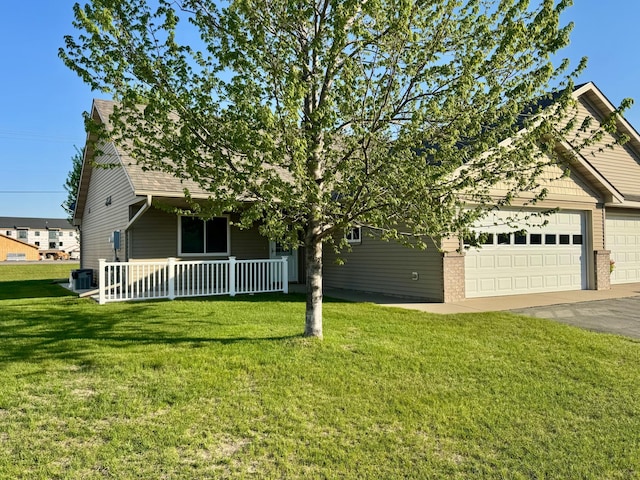 view of property hidden behind natural elements featuring covered porch, a front yard, an attached garage, asphalt driveway, and brick siding
