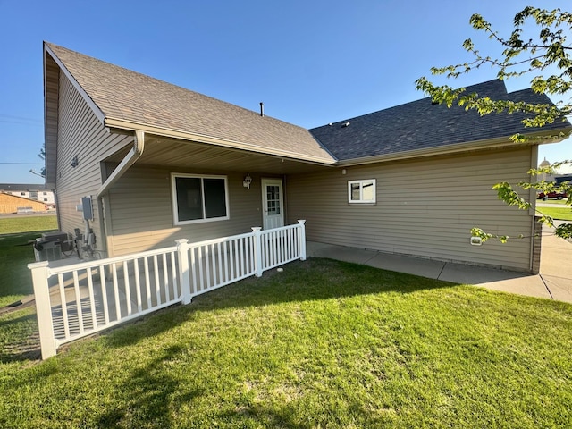back of property featuring a yard, roof with shingles, and a porch
