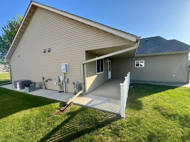 back of property with a yard, roof with shingles, and a patio area