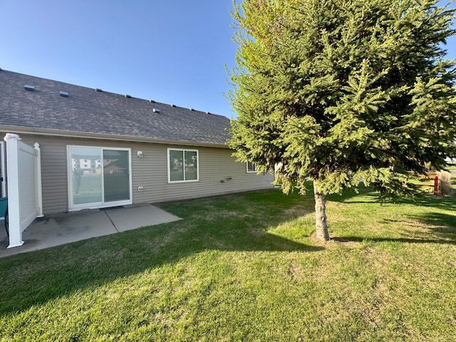 rear view of property featuring roof with shingles, a yard, and a patio area
