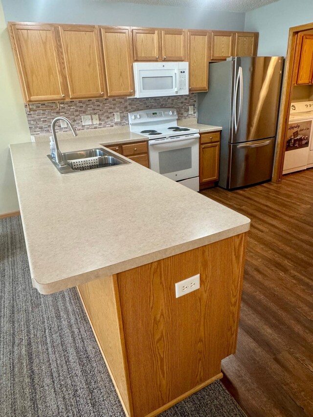 kitchen featuring white appliances, a sink, washer / clothes dryer, a peninsula, and tasteful backsplash