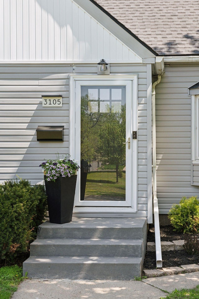 view of exterior entry featuring roof with shingles