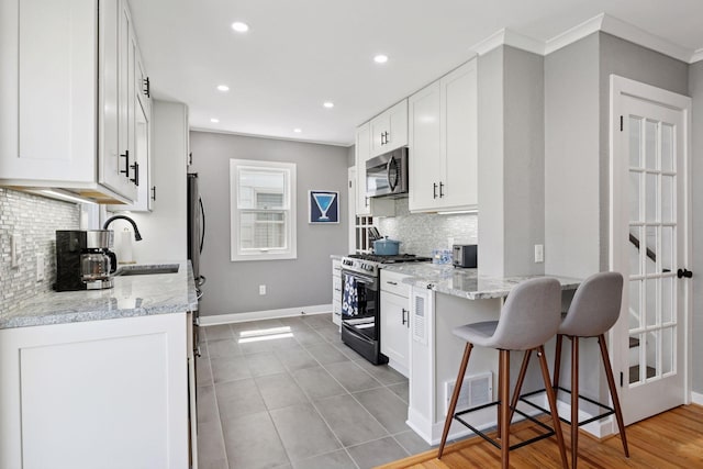 kitchen featuring appliances with stainless steel finishes, a sink, backsplash, white cabinetry, and recessed lighting