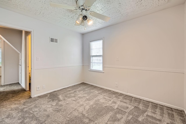 empty room with carpet flooring, a ceiling fan, wainscoting, and a textured ceiling