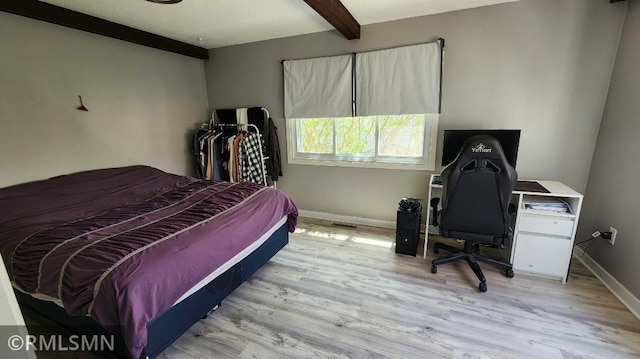 bedroom featuring light wood-style floors, beam ceiling, and baseboards