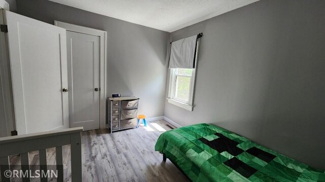 bedroom with light wood-type flooring, a textured ceiling, and baseboards