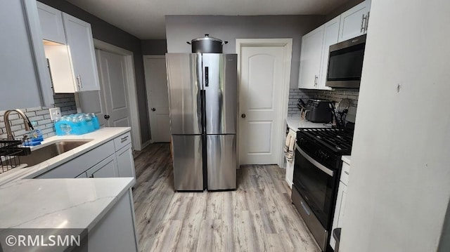 kitchen with stainless steel appliances, a sink, decorative backsplash, and light wood-style floors