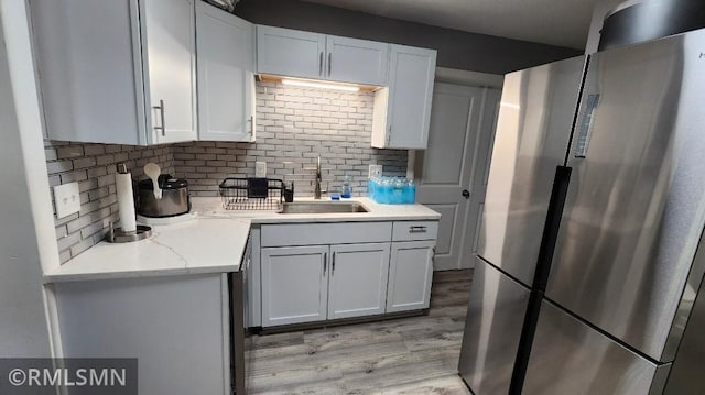 kitchen featuring freestanding refrigerator, tasteful backsplash, light wood-type flooring, and a sink