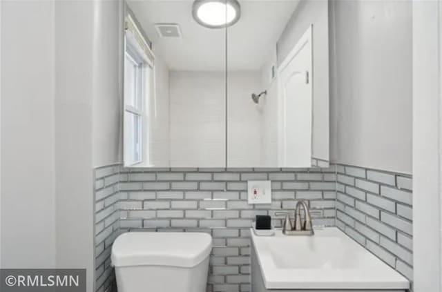 bathroom with toilet, vanity, and decorative backsplash