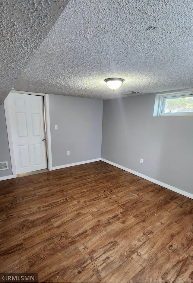 empty room with wood finished floors, a textured ceiling, and baseboards