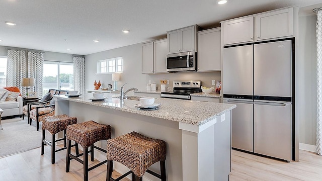3045 125th Ln NE Unit A, Blaine, MN 55449 - kitchen featuring appliances with stainless steel finishes, light wood finished floors, a breakfast bar, recessed lighting, and light stone countertops