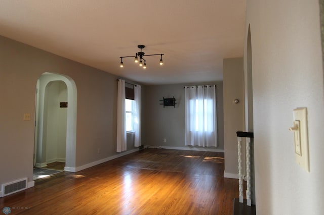 spare room featuring arched walkways, wood finished floors, and baseboards