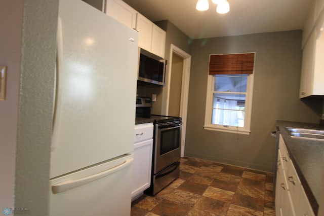 kitchen featuring stainless steel appliances, dark countertops, dark stone finish floors, white cabinets, and a sink