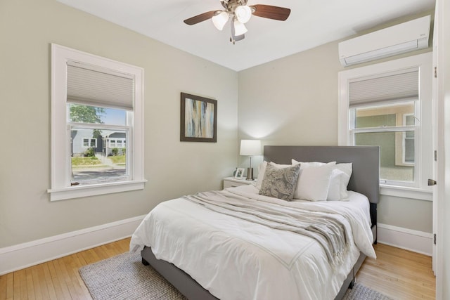 bedroom featuring an AC wall unit, wood finished floors, baseboards, and ceiling fan