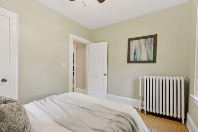 bedroom featuring radiator heating unit, light wood-style floors, and a ceiling fan