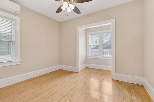 empty room featuring a wall mounted AC, light wood-style floors, baseboards, and a ceiling fan